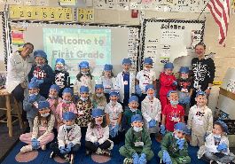  first grade students and two teachers pose for picture wearing doctors caps, gloves, and masks